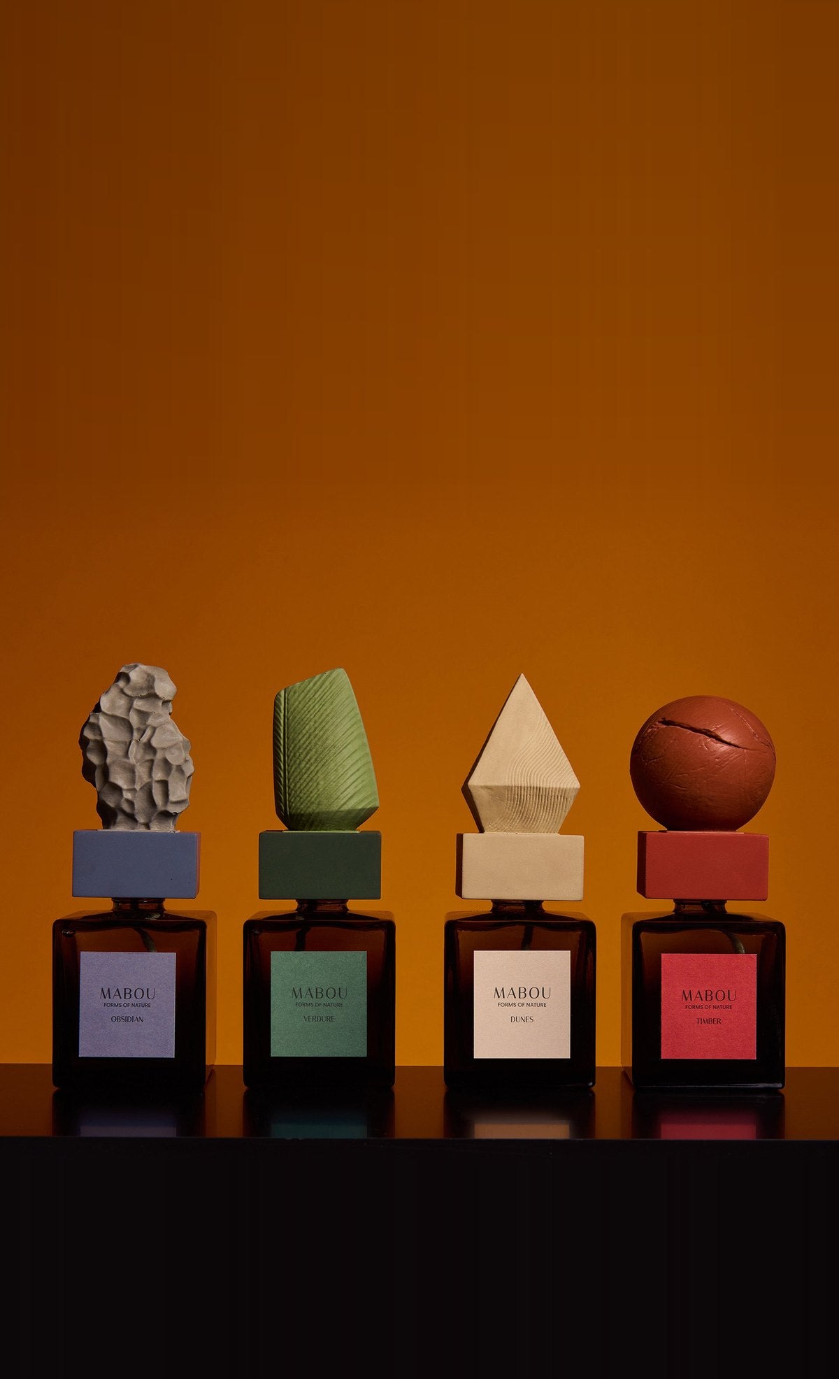 Vier Raumduft-Skulpturen der Kollektion Forms of Nature vor orangem Hintergrund